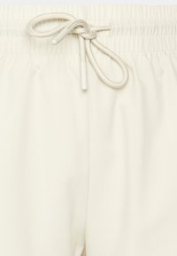 Pantalones de chándal color beige claro con cintura elástica, que cuentan con un cierre de cordón y una textura suave y lisa. Sin patrones visibles.