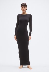 Ilga juoda suknelė iš minkštos, tamprios medžiagos. Turi ilgus rankovus ir valtis formos iškirptę, glaudžiai priglunda prie kūno su tiesia apatine kraštine.