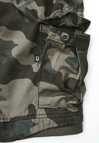 Kamufliažo rašto audinys žalių ir rudų atspalvių, išsamiai pavaizduotas su sagomis ir kišene, su mažu juodu logotipo ženkleliu.