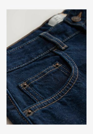 Jean en denim noir avec des coutures orange contrastantes, doté d'une poche avant avec des rivets en métal et une étiquette visible sur la taille.