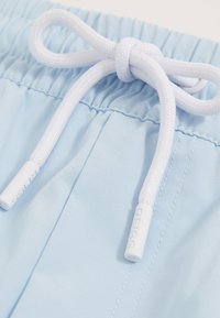 Nahaufnahme eines hellblauen elastischen Bunds mit gebundenem weißem Kordelzug an lässigen Shorts oder Hosen.