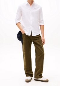 Camicia bianca con maniche arrotolate, pantaloni larghi verde oliva con tasche cargo e sneakers bianche con dettagli grigi.