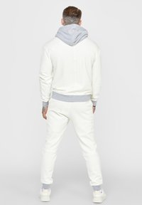 Vit hoodie med grå huva, matchande vita joggers. Tillverkad av mjukt material, med ribbade cuffs och en avslappnad passform. Minimalistisk design.