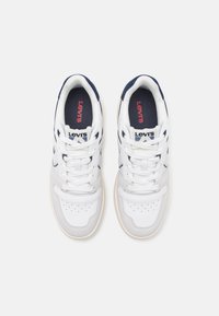 Vita sneakers med en slät läderövre, marinblå detaljer, perforerade inslag och vita snören. Har en synlig logotyp på innersulan.