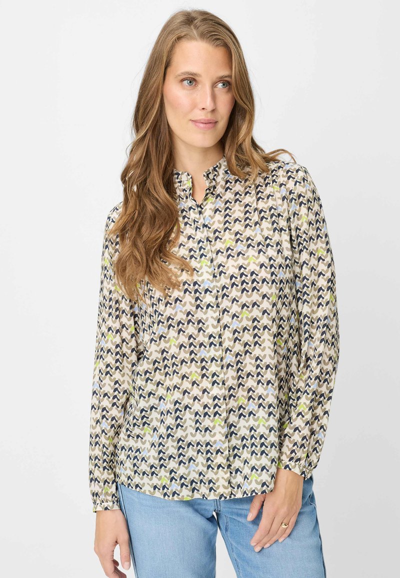 Blouse met lange mouwen, voorzien van een crèmekleurige basis met zigzagpatronen in marineblauw, olijfgroen en lichtblauw. Ronde halslijn en licht geplooide mouwen.