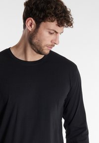 Schwarzes Langarmshirt aus weichem Stoff. Verfügt über einen runden Ausschnitt und eine taillierte Passform, mit glatter Textur und ohne sichtbare Muster oder Metallteile.