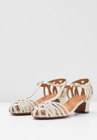Beige sandály na podpatku s pásky, s pleteným designem, malým blokovým podpatkem a T-páskem s nastavitelnou sponou. Vnitřní podšívka v hnědé barvě.