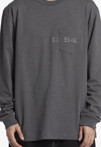 Långärmad grå skjorta i bomull, med en bröstficka med tonalt logotryck. Mjuk textur och avslappnad passform.