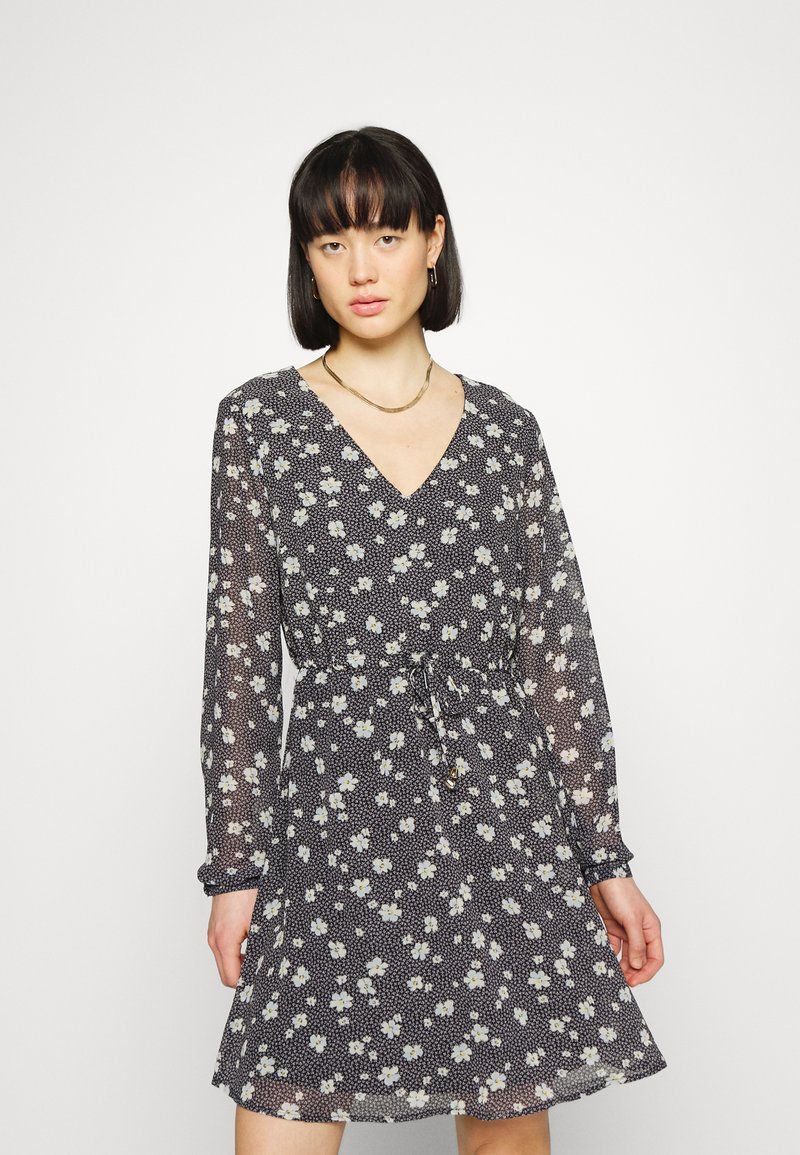 Vestido floral azul-marinho com decote em V, mangas longas e cintura ajustável. O tecido é leve e semi-transparente, com padrões de flores brancas e amarelas.