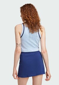 Lichtblauwe mouwloze top met donkerblauwe accenten en een marineblauwe minirok. Materialen lijken zacht met een gladde textuur. Vlindertattoo zichtbaar.