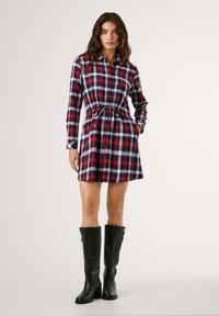 Gestreepte jurk in blauw, rood en wit, met lange mouwen en een getailleerde taille. Gecombineerd met hoge zwarte leren laarzen. Gladde textuur.