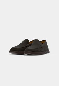 Mocassins marron foncé en matière suédée lisse. Dotés de décorations en surpiqûres et d'un design à bout rond. Modèle à enfiler, avec une semelle flexible.