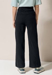 Pantalons larges noirs en tissu texturé avec une coupe décontractée, présentant une taille ajustée et des poches arrière discrètes. Associés à des chaussures légères.