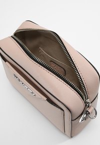 Vaaleanpunainen, teksturoitu pieni käsilaukku, jossa on hopeinen osittain auki oleva vetoketju, etutasku ja mustat reunat.