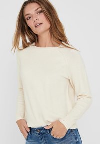 Cremfarbener Strickpullover mit Rundhalsausschnitt, gerippten Bündchen und Saum. Weicher Stoff, lange Ärmel und ein lässiger Schnitt. Kombiniert mit blauen Jeans.
