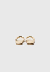 Golden flat sandals with a minimalist design, featuring an open toe and slender straps. The sole is flat and slightly textured.
