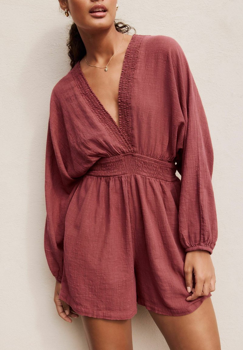 Raspberry-colored romper features a deep V-neck, smocked waist, and long balloon sleeves with gathered cuffs, made from lightweight fabric.