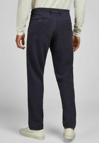 Marineblauwe broek met een relaxte pasvorm, voorzien van achterzakken met knoopsluitingen, een soepele textuur en taps toelopende enkels, gecombineerd met witte sneakers.