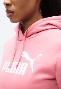 Ροζ φούτερ με κουκούλα από βαμβακερό μείγμα ύφασμα, με λευκό λογότυπο Puma και γραφικά. Διαθέτει κουκούλα με κορδόνι και ριμπ μανσέτες.