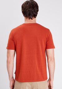 T-shirt a maniche corte color ruggine realizzato in cotone, con colletto a girocollo e taglio dritto, con dettagli di cucitura minimi sull'orlo.