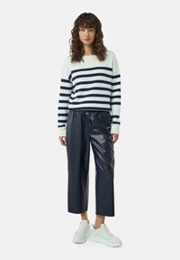 Sweter w paski w kolorze białym i granatowym; w połączeniu z czarnymi spodniami  z sztucznej skóry o kroju cropped; białe sneakersy z masywną podeszwą.
