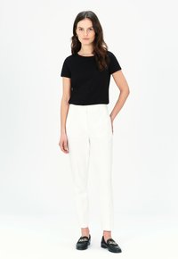 Svart kortärmad t-shirt med rund halsringning och ficka, kombinerad med vita skräddarsydda byxor. Skorna består av svarta loafers med gulddetaljer.