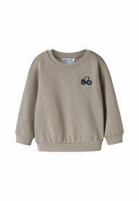 Bēšas krāsas džemperis no kokvilnas maisījuma, ar ribotu apaļu apkakli un aprocēm, uz krūškurvja neliela tumši zila traktora izšuvums.