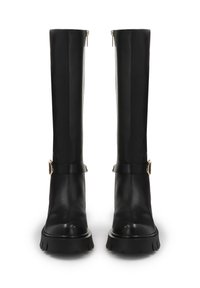 Botas de cuero negras hasta la rodilla con un acabado liso, que presentan un acento de cinturón y cremallera lateral. Suelas gruesas y con textura para durabilidad y agarre.