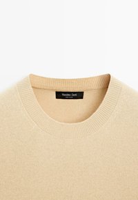 Béžový pletený svetr s žebrovaným kulatým výstřihem a měkkou texturou. Na štítku je nápis "Massimo Dutti," což značí značku původu.
