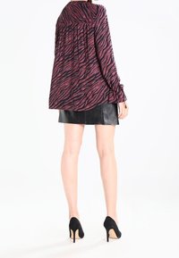Blouse ample à manches longues, rayée noir et rose foncé en motif zèbre, associée à une mini-jupe en cuir noir et des escarpins noirs à talons aiguilles.