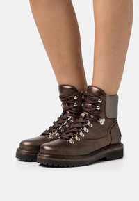 Stivali da trekking in pelle metallica marrone con lacci robusti, parti in metallo argentato e una suola resistente. Design alto alla caviglia con un colletto imbottito.