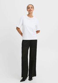 Witte katoenen T-shirt met korte mouwen, gecombineerd met zwarte gehaakte broek met wijde pijpen en een golvende zoom. Zwarte puntige schoenen.