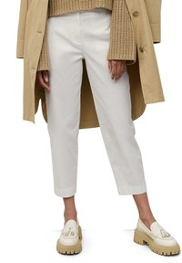 Pantalons blancs, coupés, avec une coupe ajustée, assortis à des mocassins crème avec une semelle compensée et des détails en franges. Pull en tricot beige en dessous.