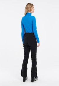 Blå långärmad tröja och svarta skidbyxor med sidodragkedjor; svarta skidboots synliga i botten. Släta material designade för vintersporter.