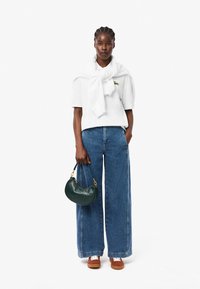 Biała koszula z krótkim rękawem, niebieskie szerokie dżinsy, brązowe sneakersy oraz ciemnozielona skórzana torebka z złotymi detalami.