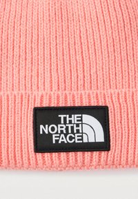Ροζ πλεκτός σκούφος με ριμπ υφή, που διαθέτει μια μαύρη ετικέτα με το λευκό λογότυπο που γράφει "THE NORTH FACE" και καμπυλωτό γραφικό σχέδιο.