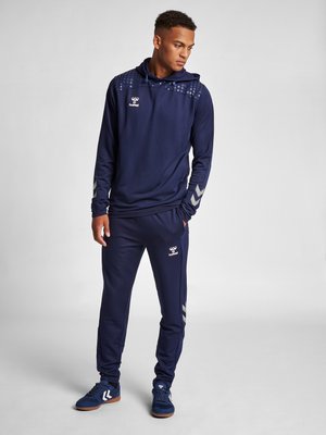 Hoodie marine avec un haut texturé, motif hexagonal et logo. Accompagné d'un jogger assorti avec des accents de rayures argentées et des chaussures de sport.