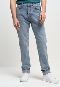 Jeans de mezclilla azul claro con un corte recto, con un lavado desgastado, presillas para el cinturón, diseño clásico de cinco bolsillos y dobladillos doblados sobre zapatillas blancas.