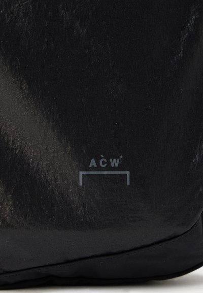 Melna auduma soma ar gludu, teksturētu virsmu un smalku spīdumu. Logo "AŌW" ir attēlots pelēkā krāsā.