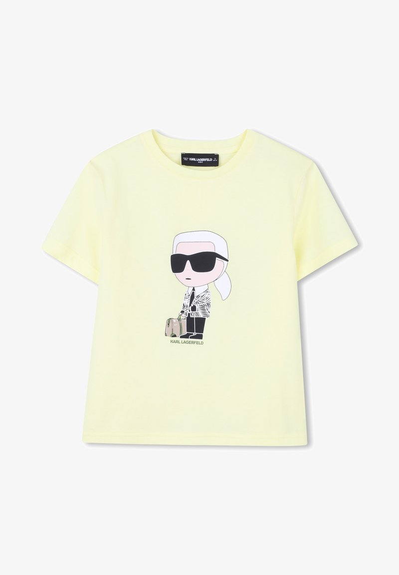 T-shirt en coton jaune avec un personnage de dessin animé aux cheveux blancs, portant des lunettes de soleil, une veste à motifs, et un petit sac, portant l'inscription "KARL LAGERFELD".