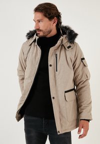 Biežs ziemas apģērbs ar kažokādas oderi kapucē, ar rāvējslēdzēju priekšpusē un vairākiem kabatām. Tam ir teksturēta auduma virsma un melni akcenti.