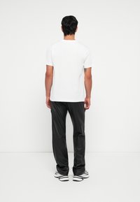 Hvit t-skjorte med korte ermer kombinert med svarte bukser i faux lær. Outfiten fullføres med svart og hvitt sneakers, sett fra bak.