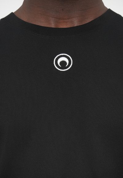 Juoda medvilninė marškinėliai su apvaliomis baltos spalvos siuvinėtomis logotipu krūtinės srityje, klasikinio dizaino su apvalia kaklo iškirpte ir lygiu paviršiumi.