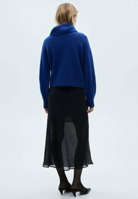 Sweter w kolorze kobaltowym, dzianinowy, z wysokim prążkowanym kołnierzem i skróconym krojem. Zestawiony z przezroczystą czarną spódnicą i czarnymi rajstopami.