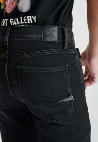 Jean en denim noir avec une coupe droite classique, comportant deux poches arrière et une étiquette en cuir texturé sur la taille.