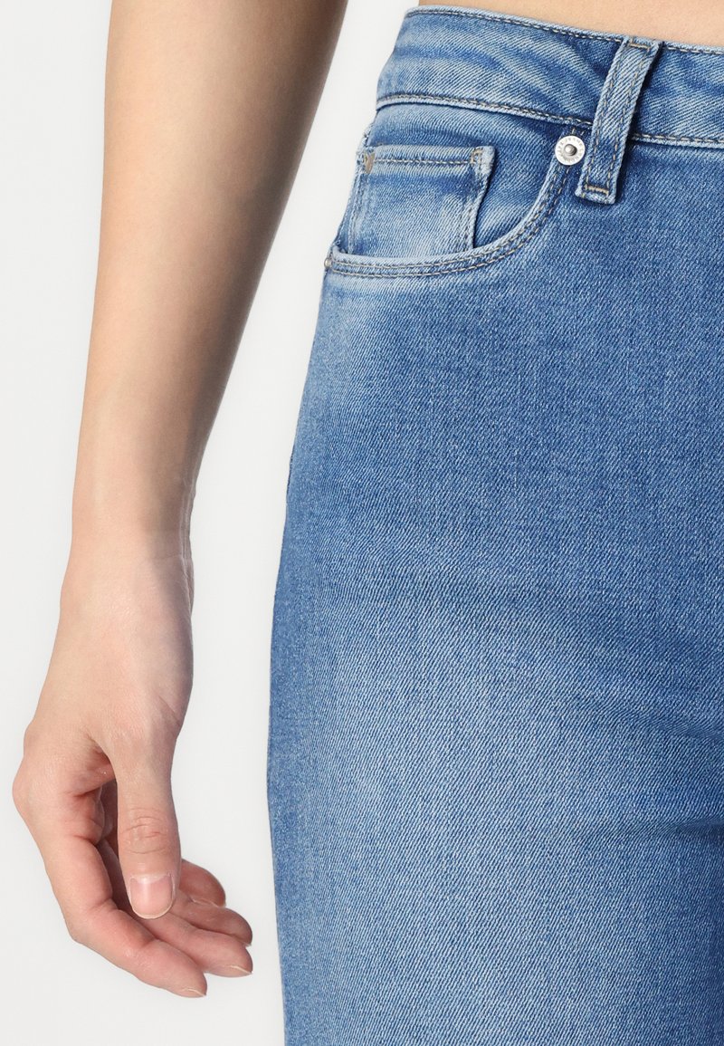 Hellblaue Denim-Jeans mit einer taillierten Passform, ausgestattet mit einer Vordertasche und einem Metallknopfverschluss. Glatte Textur mit einem dezenten Wasch-Effekt.