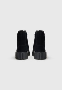 Bottines noires en daim avec une semelle en caoutchouc nervuré. Elles sont dotées d'une courte doublure en fausse fourrure et d'une languette à l'arrière pour un enfilage facile.