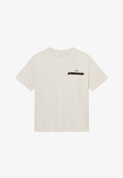 Εκρού κοντομάνικο T-shirt με στρογγυλή λαιμόκοψη, μικρό μαύρο κείμενο "W.W." και μαύρη πινελιά πινέλου στο αριστερό μέρος του στήθους.