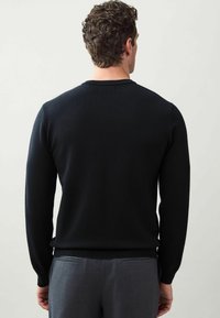 Pulover tricotat negru, cu gât rotund, mâneci lungi și tiv zimțat. Purtați peste pantaloni gri, asortați, evidențiind un material texturat.