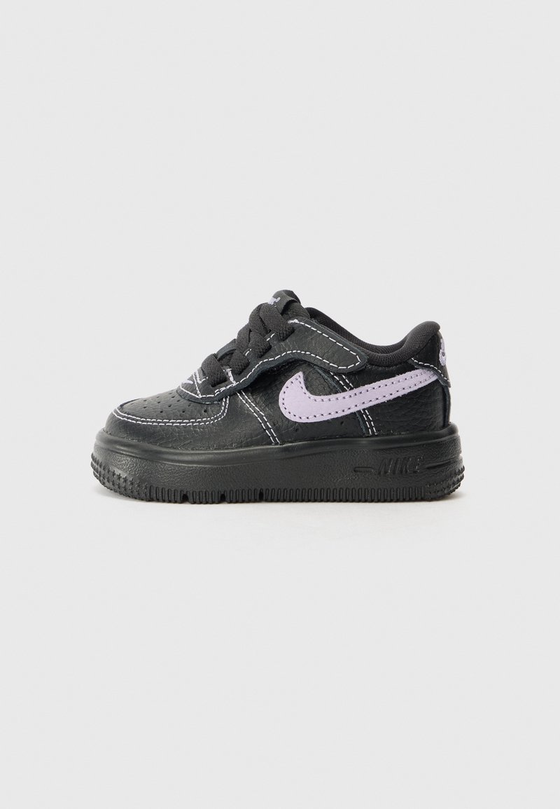 Baskets noires Nike avec semelle épaisse, logo swoosh violet, lacets noirs et coutures blanches, vues de profil sur fond uni.